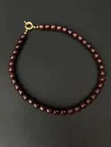 Collar de cuentas de sugilita natural en tonos violeta oscuro, con cierre de mosquetón en acabado dorado.