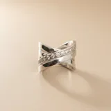 Anillo de plata 925 con diseño cruzado, compuesto por bandas lisas y una banda central engastada con pequeñas circonias brillantes.