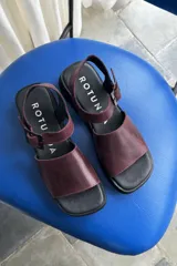 Sandalias de cuero color bordó, con suela plana y gruesa de goma negra, tira ancha en el empeine y tira ajustable con hebilla en el talón.