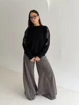 Sweater negro de tejido de punto con cuello redondo y mangas largas. Presenta detalles de transparencias y apliques bordados con pedrería en la parte superior de las mangas.