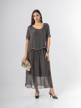 Vestido largo de seda italiana en color gris oscuro, con falda larga lisa, forro y cintura elastizada. Posee una sobrecapa con detalles de paillettes en los bordes de las mangas y la cintura.