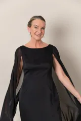 Vestido largo de crepe negro, con capa de gasa que sale de los hombros y abertura en la espalda.