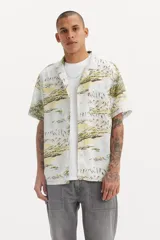 Camisa de hombre de manga corta con cuello clásico y estampado de paisaje con palmeras y montañas en tonos blanco, amarillo y verde.
