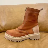 Bota de cuero color marrón terracota, con caña media, cierre frontal con cremallera y suela track color beige.