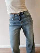 Pantalón de jean con corte wide leg y tiro medio-alto. Presenta un lavado gris azulado desgastado con acabado vintage y ruedo desflecado.