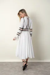 Vestido midi blanco con detalles de encaje y vivos negros. Tiene cuello mao, mangas largas con puños de encaje y falda amplia con tul de armar.