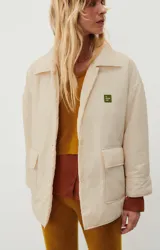 Chaqueta capitoneada color crema, de corte oversize, con cuello camisero, cierre frontal con botones a presión, bolsillos de parche y puños con abertura.