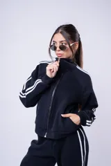 Campera tipo bomber color negro con cuello alto y cierre frontal. Presenta dos líneas blancas paralelas a lo largo de las mangas y puños elásticos acanalados.