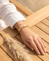 Esclava rígida de acero con baño de oro, decorada con cinco dijes de ojo turco incrustados. Se presenta junto a una pulsera de cadena fina con un dije de mano de Fátima.