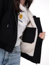 Chaqueta negra de lona con forro interior de sherpa, cierre frontal con cremallera, capucha ajustable con cordón y puños y bajo de punto acanalado.