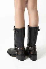 Bota de caña media confeccionada en cuero con efecto gastado manual. Presenta punta cuadrada, taco bloque y detalle de tira con hebilla en la parte superior de la caña, además de una tira decorativa con argolla metálica y remaches en la zona del tobillo.