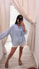 Camisa oversize color verde militar con finas rayas verticales de lurex, cuello camisero y mangas largas con puños anchos.