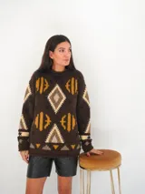 Sweater de tejido de punto grueso con diseño geométrico estilo étnico en tonos marrón, mostaza y beige. Presenta cuello redondo, mangas largas y terminaciones en punto elástico acanalado.