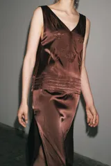 Vestido midi marrón con bordados florales y geométricos en el frente, escote redondo, mangas sisa, tejido plisado y flecos en el ruedo.