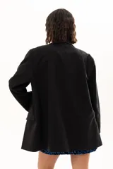 Blazer negro de corte oversize con solapas clásicas, cierre frontal de doble botonadura y bolsillos laterales con solapa.