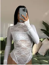 Body de encaje blanco con cuello alto y mangas largas de microtul. Presenta un diseño entallado con detalles de puntilla en los puños y en el borde inferior, combinando transparencias y texturas delicadas.