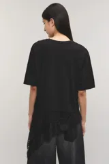 Remera negra de corte oversize, con escote redondo, mangas cortas y detalle de tajo irregular con terminación en puntilla en el ruedo. Confeccionada en jersey de algodón.