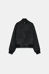 Cazadora bomber gris oscuro de corte holgado, confeccionada con hilatura de lana. Presenta cuello subido, manga larga, bolsillos delanteros y acabados de canalé negro en cuello, puños y ruedo. Cierre frontal con botones negros.