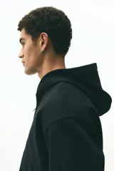 Campera con capucha de felpa pesada, con cierre frontal, bolsillos laterales y puños y bajo acanalados. Presenta un corte holgado y diseño minimalista.