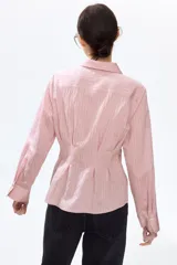 Camisa entallada de mezcla de viscosa en color rosado, con efecto arrugado y bajo levemente acampanado. Presenta cuello camisero, cierre frontal de botones, canesú en la espalda y pliegues en la cintura que definen la silueta. Cuenta con mangas largas y puños abotonados.
