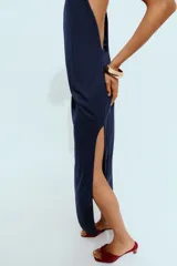 Vestido midi de tejido elástico color azul marino, con cuello halter, aberturas en la espalda y detalle de aplique metálico.
