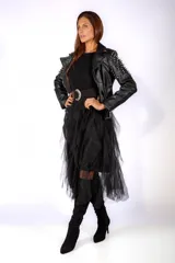 Chaqueta tipo biker de cuero sintético negro, con solapas amplias, cierre frontal asimétrico y detalles de tachas metálicas en las mangas. Incluye cinturón con hebilla en el ruedo.