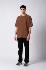 Remera de corte oversized en color marrón, confeccionada en tejido de algodón con textura de micropanal. Presenta cuello redondo con detalle de costura en forma de X y mangas cortas de estilo caído.