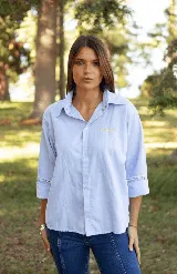 Camisa de lino color celeste, con cuello clásico, cierre frontal de botones y detalle de cuatro estrellas bordadas en color amarillo sobre el pecho. Presenta mangas tres cuartos con detalle de encaje en los puños.