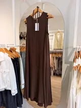 Vestido largo sin mangas de color marron con textura en relieve, de corte fluido, con tiras finas para anudar al cuello y bolsillos laterales.