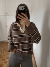 Sweater de punto marrón con diseño de rayas horizontales blancas y marrones oscuras, con cuello polo en color marfil, manga larga y corte holgado.