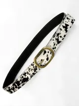 Cinto de cuero de pelo con estampado animal print tipo vaca en color blanco y negro, con hebilla metálica ovalada en tono bronce viejo con la marca grabada.