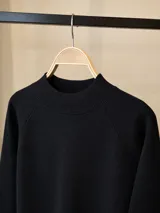 Buzo de punto en color beige, con cuello redondo alto y mangas largas con diseño raglán. Presenta puños y cuello acanalados.