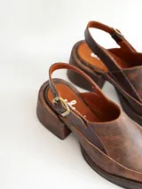 Zapato tipo zueco de cuero color chocolate con efecto desgastado, plataforma y taco cuadrado. Presenta una tira trasera ajustable con hebilla metálica.