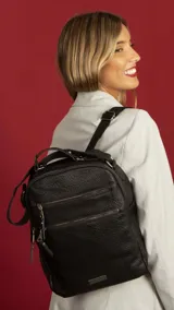 Mochila de cuero sintético con textura granulada, color negro. Cuenta con doble compartimento superior con cierre, dos bolsillos frontales con cierres metálicos, asa superior rígida y correas ajustables de cinta.