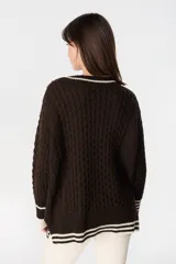 Sweater de punto estilo preppy en color crudo con detalles en marrón. Presenta cuello en V con ribete a rayas, tejido con textura de ochos y cordones laterales decorativos. Posee puños y ruedo acanalados con diseño a rayas.