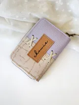 Billetera pequeña de cuero color lila y beige con cierre metálico y detalle de cordones cruzados en el frente.