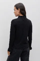 Remera de manga larga color blanco, confeccionada en tejido liviano con caída fluida. Presenta cuello alto con volados, abotonadura frontal decorativa y detalles de volados a lo largo de la abertura, además de terminaciones con volados en los puños.