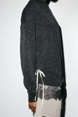 Vestido de cuello redondo y manga larga, confeccionado en tejido de punto gris oscuro. Presenta un bajo en contraste de color beige con detalle de encaje floral negro y lazada lateral ajustable.
