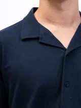 Camisa de manga corta color beige, confeccionada en tejido piqué de algodón, con cuello cubano y un bolsillo de parche en el pecho.