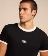 Remera blanca de algodón, modelo baby tee, con mangas cortas, cuello redondo y detalles contrastantes en marrón. Presenta un pequeño logo gomoso con la palabra "Lucky" en el centro del pecho.