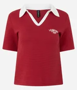 Blusa tipo polo de manga corta, color rojo, con cuello y escote en V con bies blanco contrastante. Presenta una textura gofrada y un bordado pequeño en el pecho con el texto "LE SPORT Paris".
