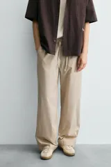 Pantalón relaxed fit color beige con rayas verticales finas, confeccionado en tejido de algodón. Cuenta con cintura elástica ajustable con cordón, bolsillos frontales y bolsillos traseros de plastrón.