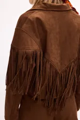 Chaqueta de efecto gamuza en color tostado, con solapas amplias, cierre frontal con un botón y flecos largos decorativos en la parte frontal y trasera de las mangas. Presenta una estructura definida y forro interior.