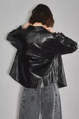 Campera de cuero sintético negro con acabado brillante, diseño tipo camisa con cuello clásico, cierre frontal con botones a presión y bolsillos delanteros. Cuenta con forro interior de algodón.