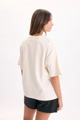 Remera manga corta de corte boxy en color crudo, con cuello redondo y estampa frontal con la palabra "BONHEUR" en tonos verdes y celestes.