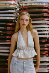 Top crop de cuello halter con escote profundo en V, confeccionado en tejido con acabado metalizado brillante. Presenta un diseño con volados en la parte inferior y lazada ajustable en la espalda.