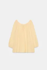 Blusa de lino color amarillo claro, con escote recto ajustable mediante lazadas, hombros descubiertos y mangas largas abullonadas con puños elásticos.