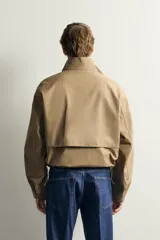 Cazadora regular fit de la colección Aaron Levine x ZARA, confeccionada en tejido con mezcla de algodón con patrón de cuadros pequeños en tonos beige y marrón. Cuenta con cuello subido, manga larga con puño ajustable con botón a presión, bolsillos de vivo en la cadera, bajo ajustable con elástico en los laterales y cierre frontal con cremallera.