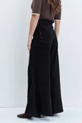Jeans de tiro alto en color negro, con diseño de corte acampanado y paneles godet que aportan amplitud en el bajo. Presenta costuras visibles y cierre frontal con botón y cremallera.