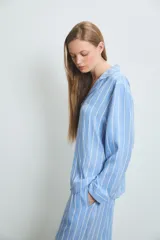 Pijama de dos piezas confeccionado en viscosa, compuesto por una camisa de manga larga con cuello solapa y cierre frontal de botones, y un pantalón de corte recto y holgado. Presenta un diseño de rayas verticales en tonos azul y blanco.
